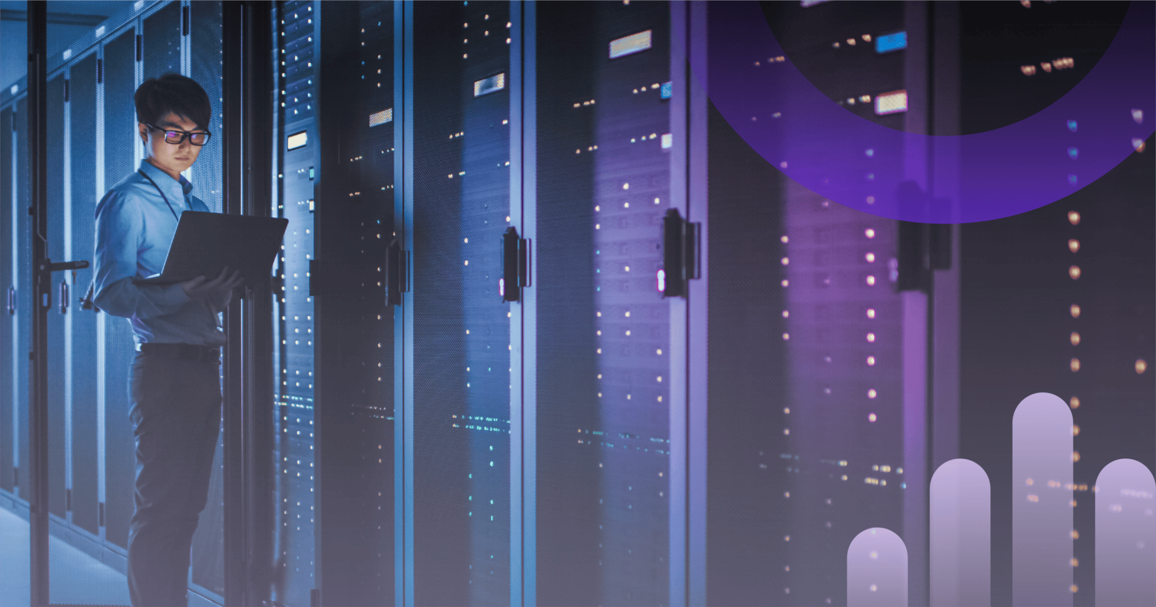 Image shows man standing in a server room holding a laptop.